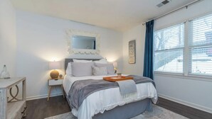 Une chambre bien rangée, avec un lit, des tables de chevet, un miroir et une fenêtre avec des rideaux.