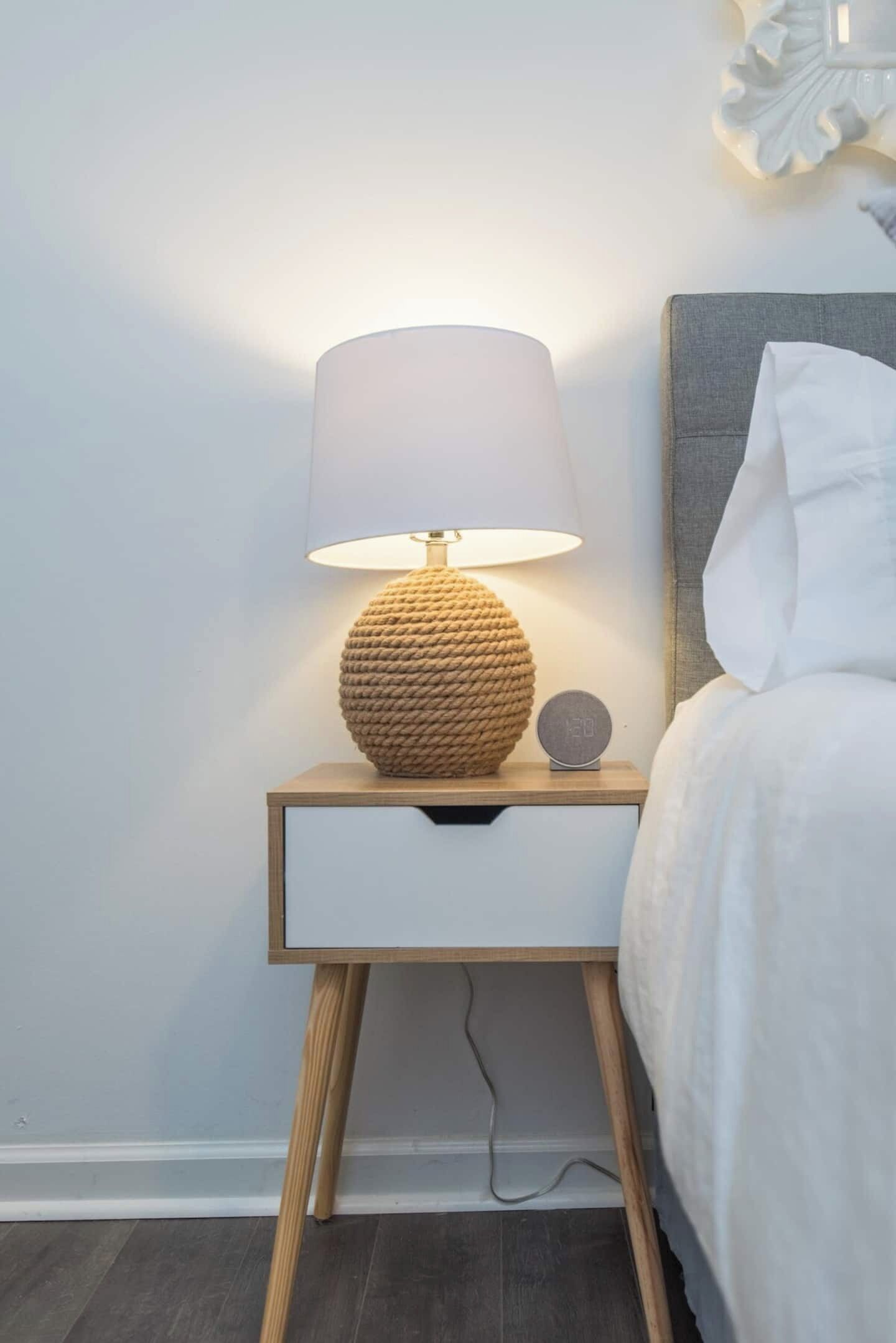 Een nachtkastje met een lamp met structuur, een klein klokje en een lade.