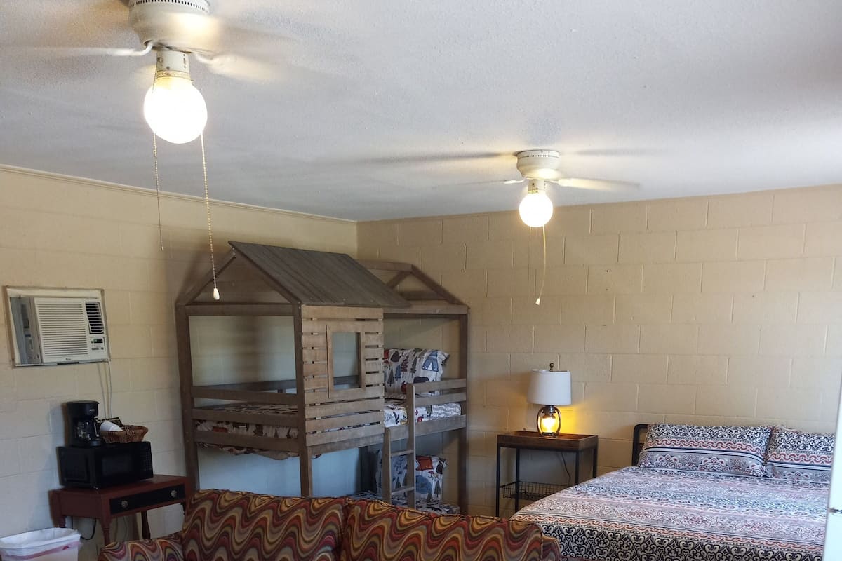 A room with bunk beds, a sofa, a table, and a lamp.