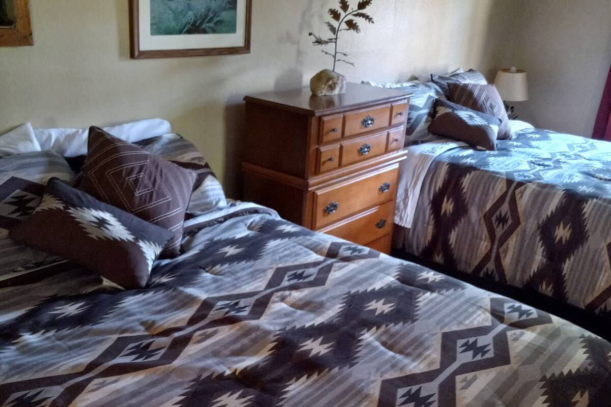A hotel room with two beds, a dresser, a framed picture on the wall, and a lamp on the nightstand.