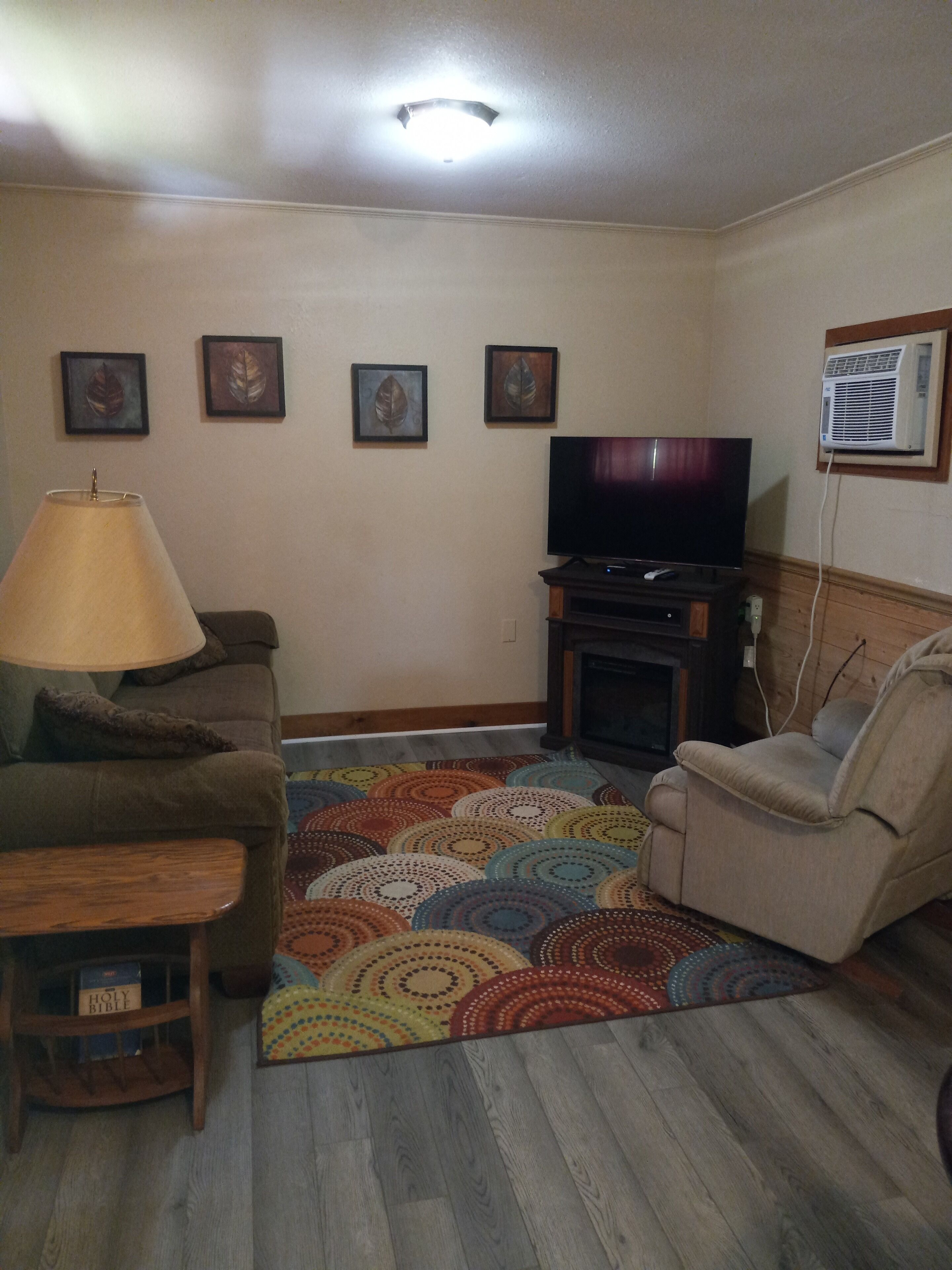 Ein Wohnzimmer mit einer Couch, einem Fernseher, einer Lampe und einem gemusterten Teppich.