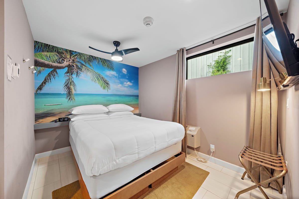 Een slaapkamer met een bed, een plafondventilator, een aan de muur bevestigde televisie en een raam met gordijnen.