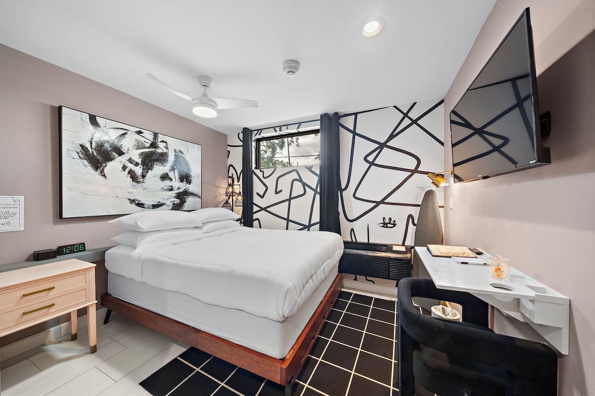 Een moderne slaapkamer met een bed, bureau, stoel en kunstwerk.