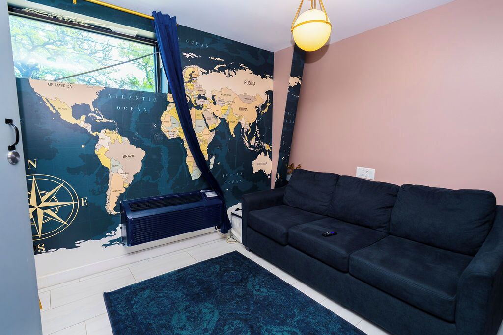 Ein Zimmer mit einer großen Weltkarte an der Wand, einem schwarzen Sofa, einem blauen Teppich und einem Fenster mit Vorhängen.