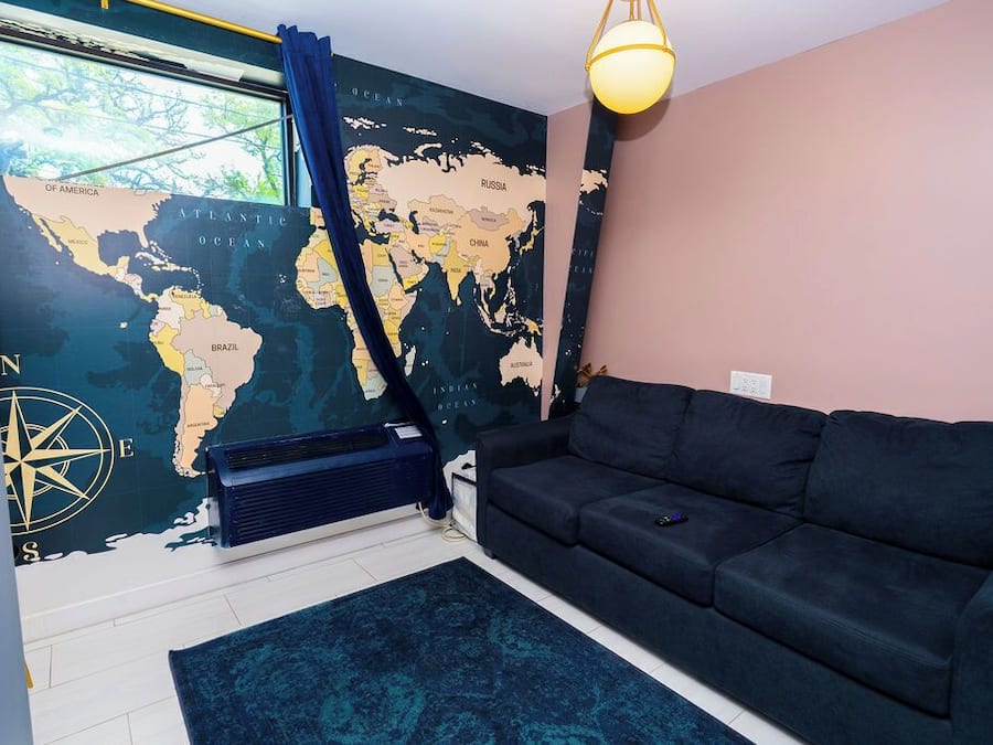 Ein Zimmer mit einer großen Weltkarte an der Wand, einem schwarzen Sofa, einem blauen Teppich und einem Fenster mit Vorhängen.