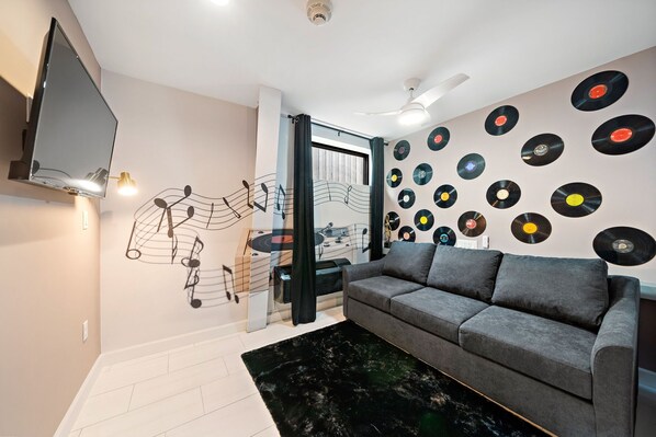 A modern living room with a grey sofa, a black rug, a wall with vinyl records, and a TV mounted on the wall. - Wanderstay Boutique Hotel (Houston)