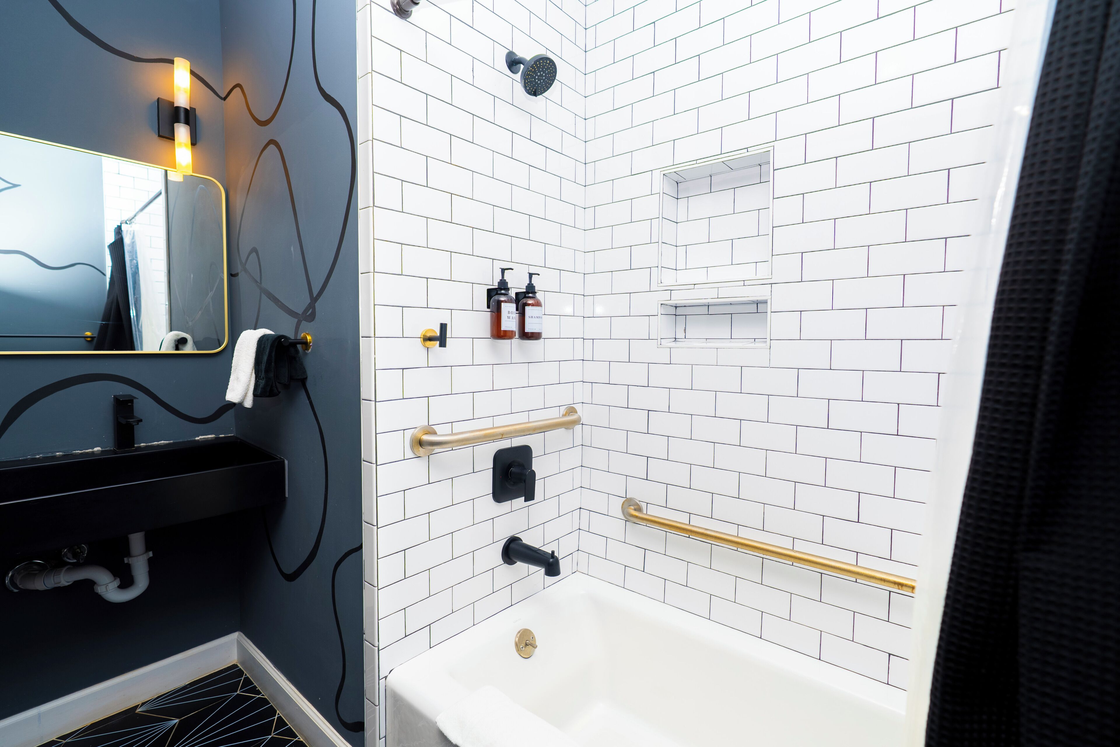 Un baño con una bañera blanca, un lavamanos negro, un espejo y un cabezal de ducha.