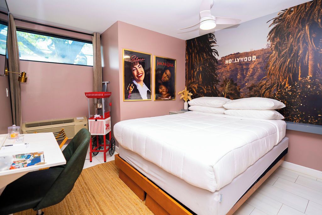 Un dormitorio con cama, escritorio, silla, radiador y un cartel grande del cartel de Hollywood.