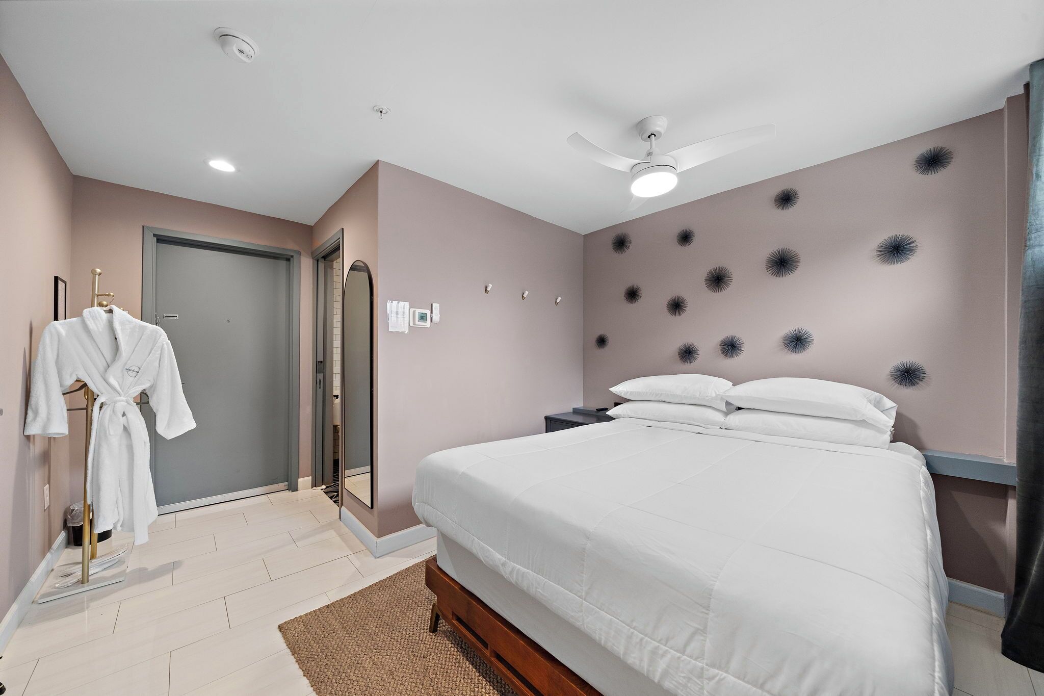 Un dormitorio con cama, perchero, ventilador de techo y una pared decorada.