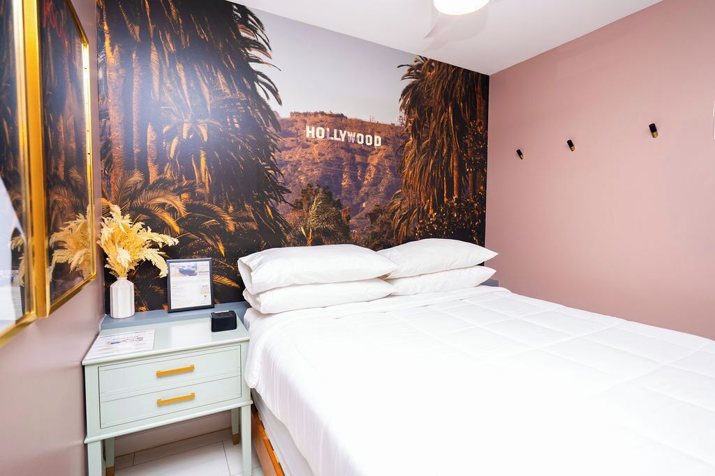 Une chambre avec un lit, une table de chevet, un miroir et un mur orné d’une fresque représentant le panneau Hollywood.