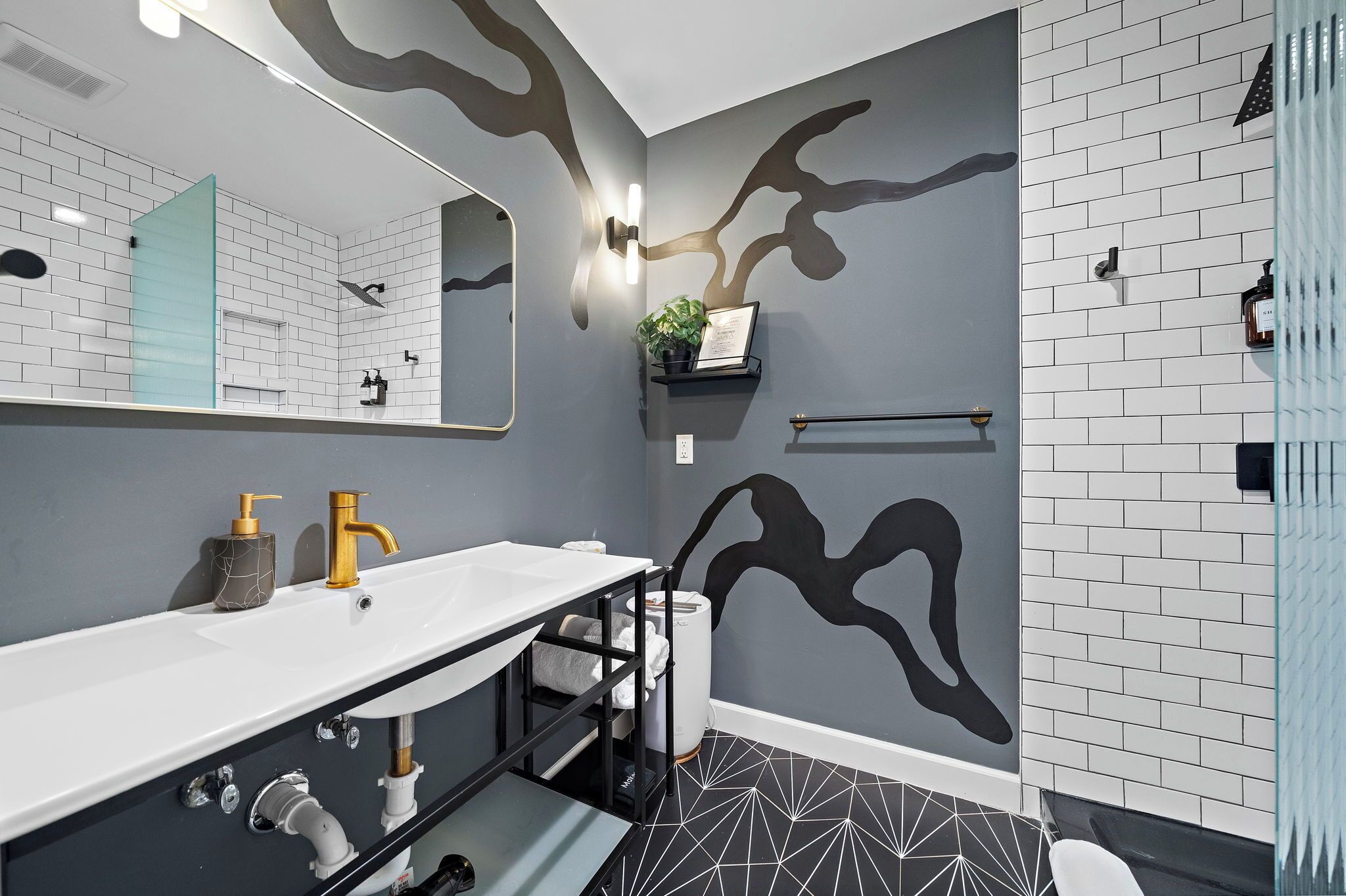 A modern bathroom with a white sink, gold faucet, and a black and white geometric floor.