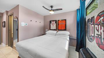 A hotel room with a bed, a ceiling fan, a window with curtains, and sports memorabilia on the wall.