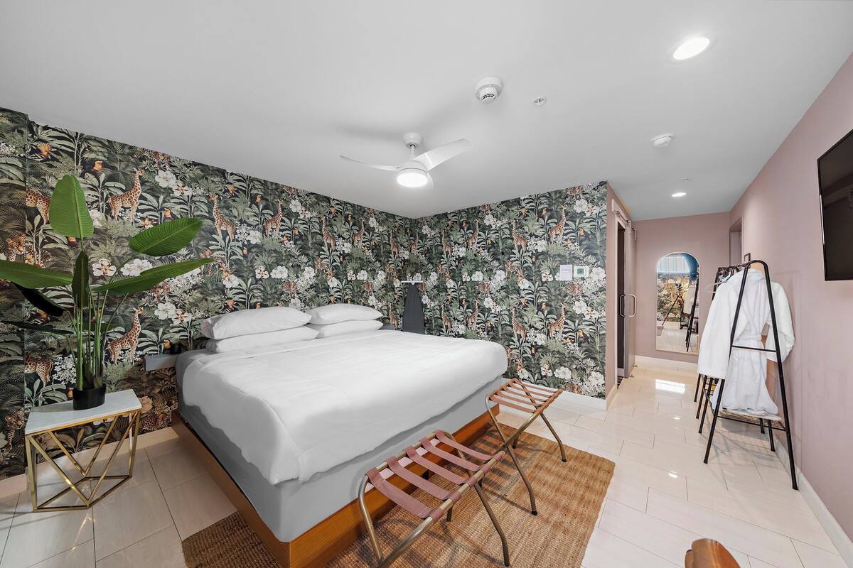Een moderne slaapkamer met een groot bed, een plafondventilator en uitzicht op een tuin door een open deur.
