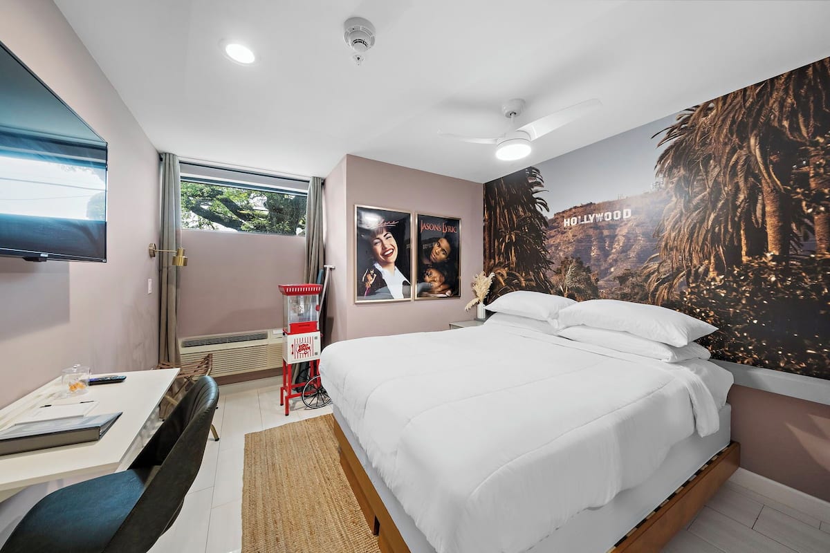 Een hotelkamer met een groot bed, een bureau met stoel, een televisie en posters aan de muur.