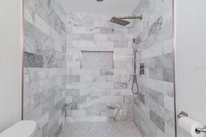 A walk-in shower with a glass door, marble tiles, and a handheld showerhead. - Fabulous Newly Renovated Mid-Century Home on Eden Isle / Snell Isle! (St. Petersburg)