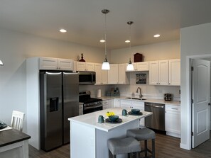 Una cocina moderna con armarios blancos, electrodomésticos de acero inoxidable e iluminación colgante.
