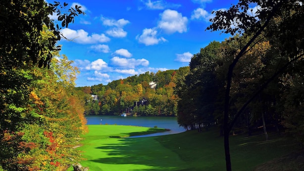 A golf course with a lake, surrounded by trees and houses.