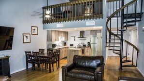 A spacious living area with a leather sofa, dining table, and chairs, a kitchen with wooden cabinets, and a spiral staircase.