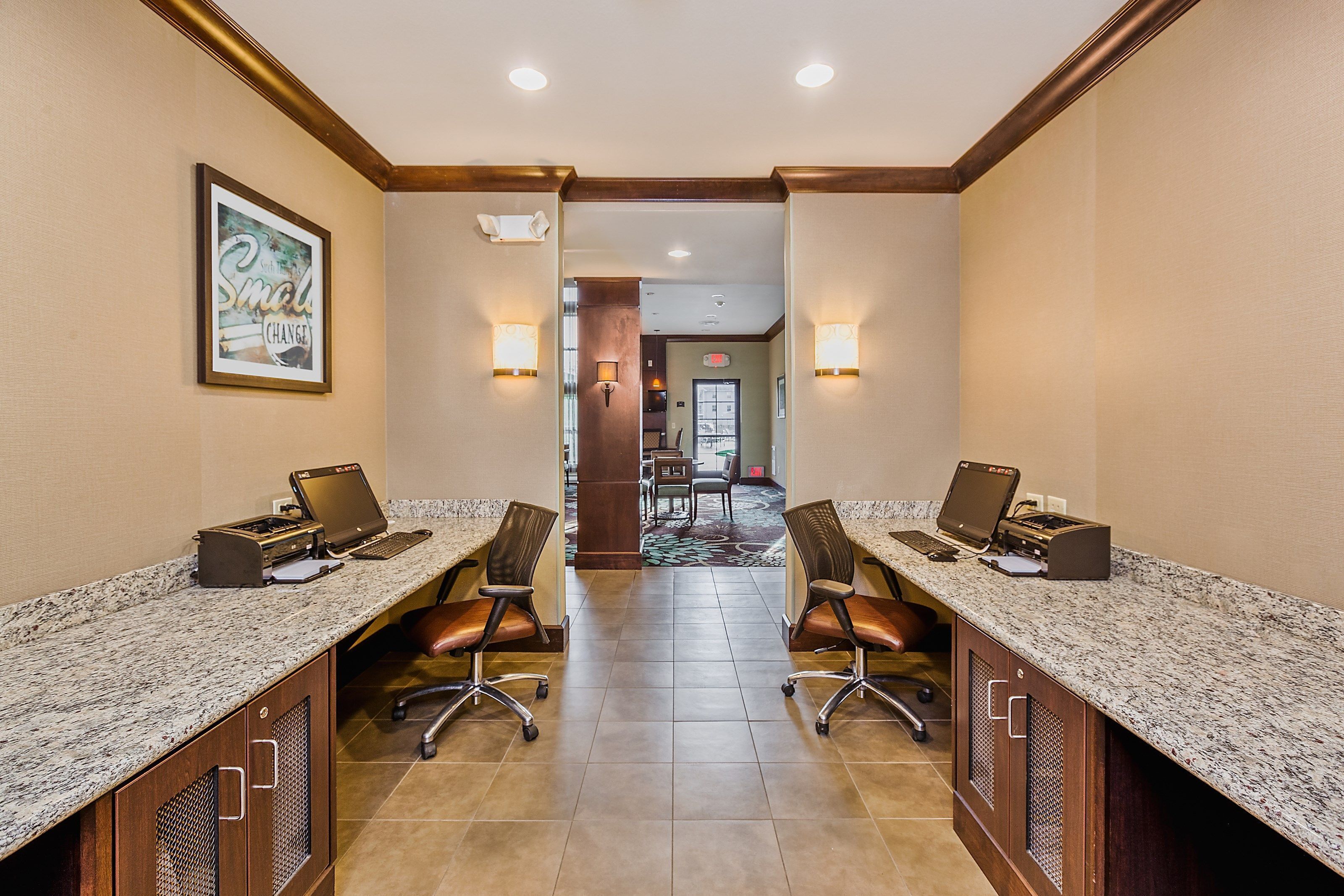 A conference room with two desks, each equipped with a laptop and a printer. The room has a carpeted floor and is well-lit with wall-mounted lamps.
