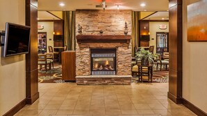 A lobby with a stone fireplace, a television mounted on the wall, and a seating area with chairs and a table.