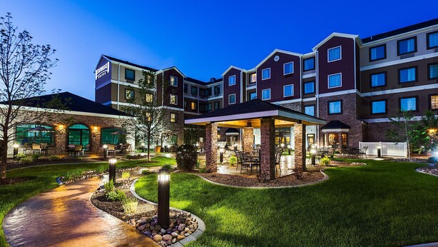 A multi-story hotel with a covered patio area, outdoor seating, and a well-maintained lawn.