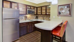 A modern kitchen with stainless steel appliances, dark wooden cabinets, a tiled backsplash, and a bar area with a red cushioned chair.