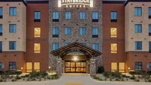A Staybridge Suites hotel with a brick facade, large windows, and a prominent entrance with a wooden archway.