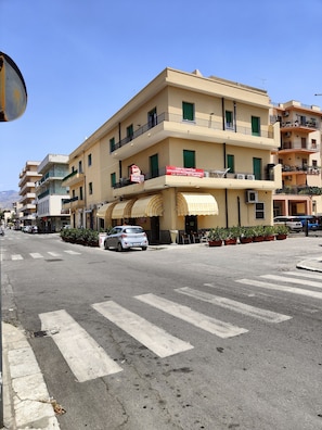 A multi-story building with balconies, a crosswalk, and parked cars.