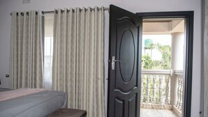 A bedroom with a bed, a window with curtains, and a door leading to a balcony. - Luxurious Two Bedroom Double Storey Apartments (Lusaka)