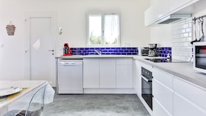 A modern kitchen with white cabinets, a blue-tiled backsplash, a dishwasher, a coffee maker, and a stove. - Le Gois - Jardin -  Marais salants (Beauvoir-sur-Mer)