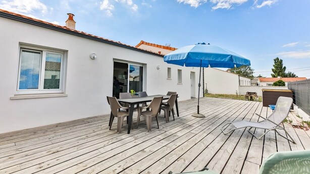 A patio with a table and chairs, a blue umbrella, and a wooden deck. - Le Gois - Jardin -  Marais salants (Beauvoir-sur-Mer)