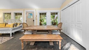 A room with a large wooden table, a white sofa with yellow cushions, and a view of a garden through a glass door. - Bird House Countryside Pecan Farm 6acre San Marcos (Maxwell)