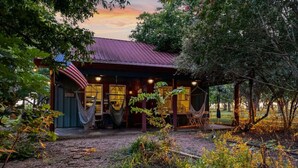 A rustic cabin with a metal roof, a hammock, and a small porch area. - Bird House Countryside Pecan Farm 6acre San Marcos (Maxwell)