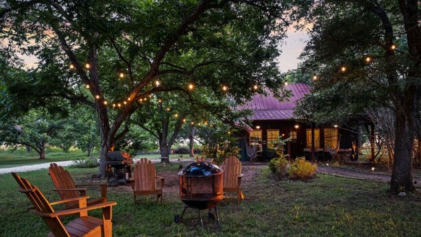 An outdoor seating area with wooden chairs, a grill, and string lights under trees. - Bird House Countryside Pecan Farm 6acre San Marcos (Maxwell)