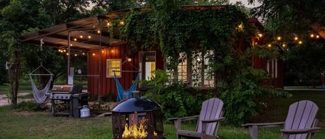 A covered outdoor seating area with a grill, chairs, and a fire pit.