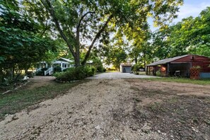 A gravel driveway leading to a rustic cabin with a covered porch and a small shed.