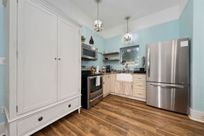 Una cocina con armarios blancos, electrodomésticos de acero inoxidable, suelo de madera e iluminación colgante.