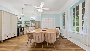 A spacious kitchen with a large dining table, white cabinets, and a ceiling fan. - RoosterHouse Countryside Pecan Farm 6ac SanMarcos (Maxwell)