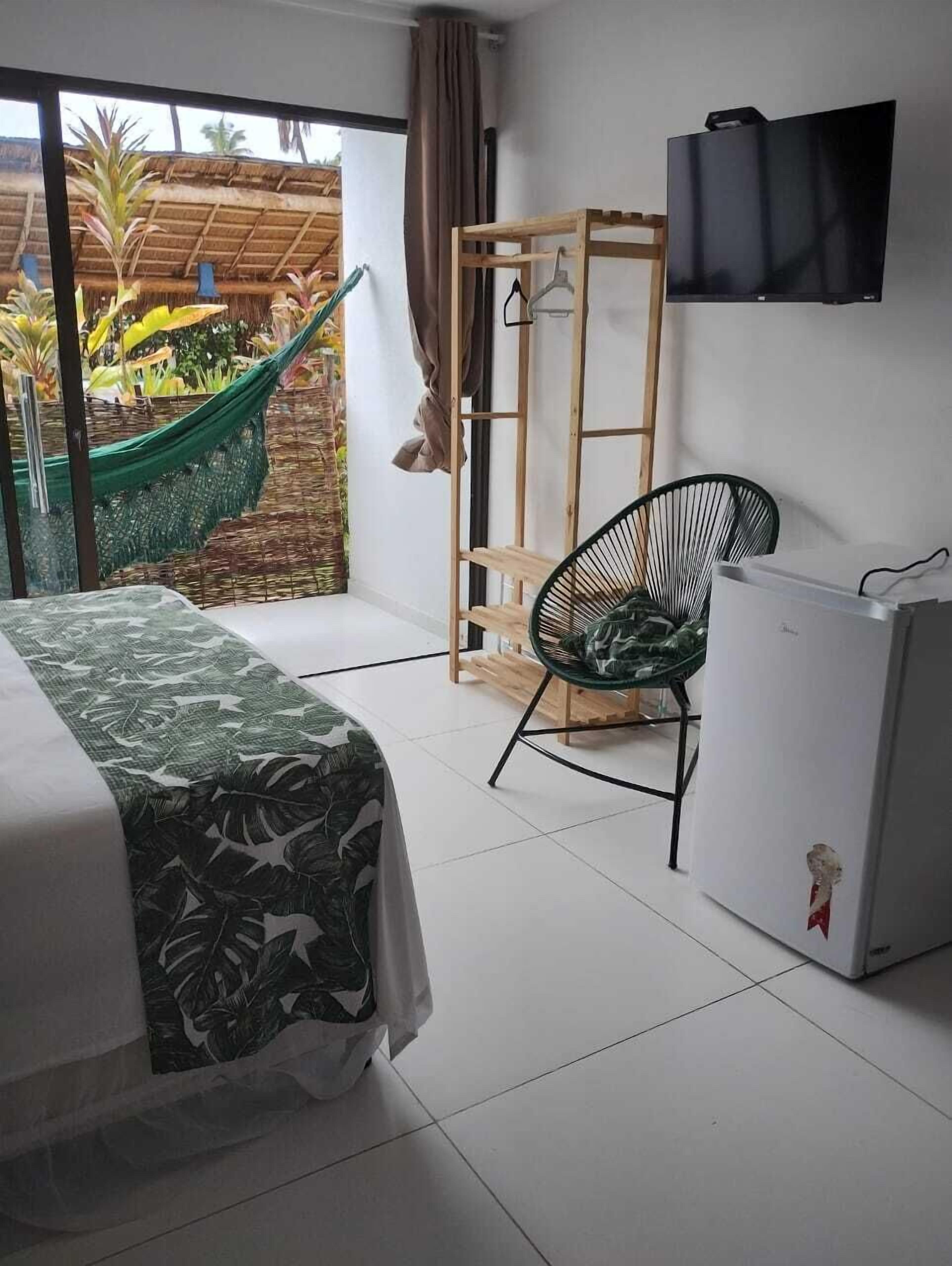 A room with a bed, a chair, a TV, and a small refrigerator.