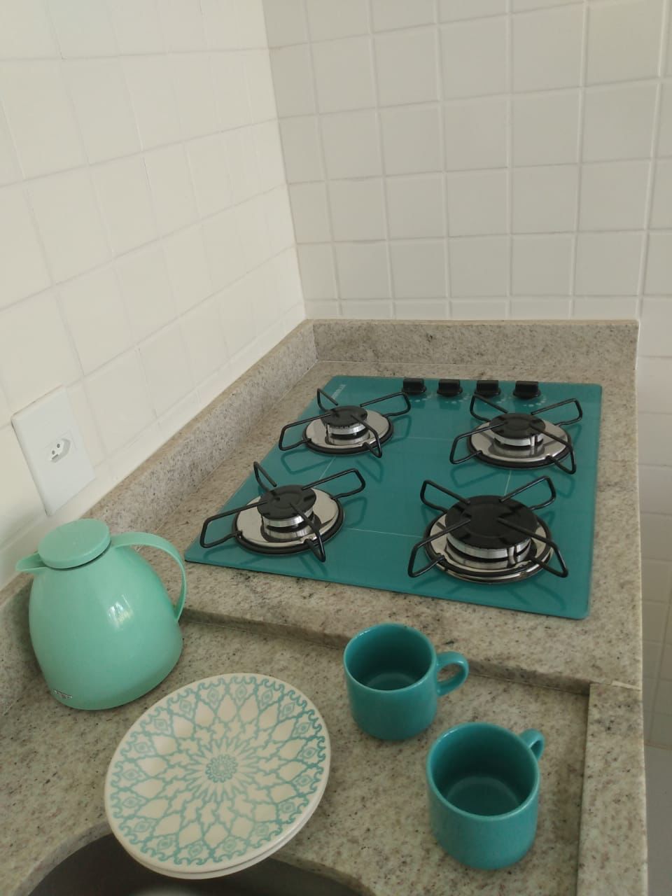 A kitchen with a gas stove, a kettle, and two mugs on a granite countertop.