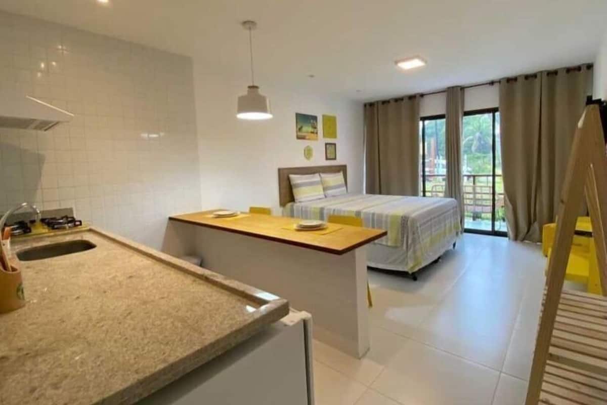 A compact hotel room with a kitchenette, a bed, and a balcony.