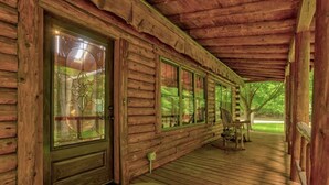 Eine Blockhütte mit überdachter Veranda, großen Fenstern und Blick auf den umliegenden Wald.