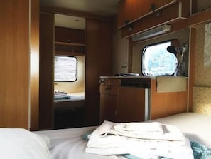 Un intérieur de camping-car compact comprenant un lit, une petite kitchenette et une fenêtre donnant sur l’extérieur.
