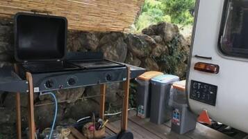A portable grill with a lid open, placed on a wooden cart next to a white vehicle.