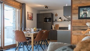 Eine moderne Küche mit grauen Schränken, einem eingebauten Backofen und einem Essbereich mit Holztisch und braunen Stühlen.