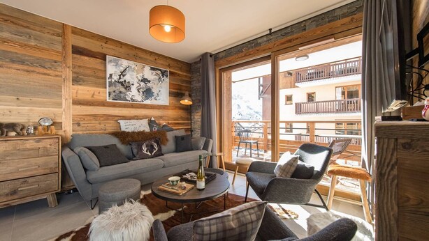 Ein gemütliches Wohnzimmer mit Holzvertäfelung, einer Couch, einem Couchtisch und Blick auf einen Balkon mit Sitzgelegenheit.