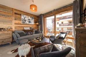 A cozy living room with a wooden interior, a sofa, a coffee table, and a view of a balcony with outdoor seating.