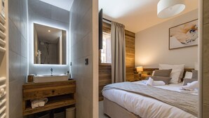Ein modernes Badezimmer mit großem Spiegel, Waschbecken und Holz-Waschtisch. Der Raum verfügt über ein großes Bett mit vielen Kissen und einer Nachttischlampe.
