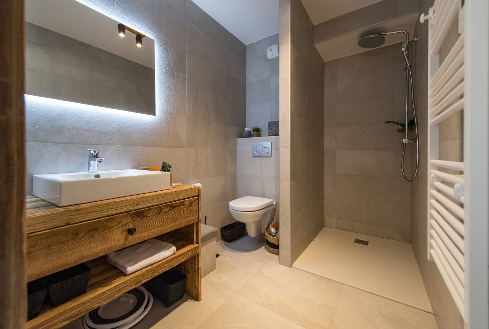 A modern bathroom with a wooden vanity, a sink, a toilet, and a shower area.