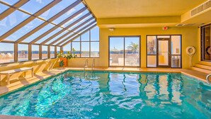Une piscine intérieure avec des parois en verre transparent, donnant sur le désert, et une porte menant à l’extérieur.